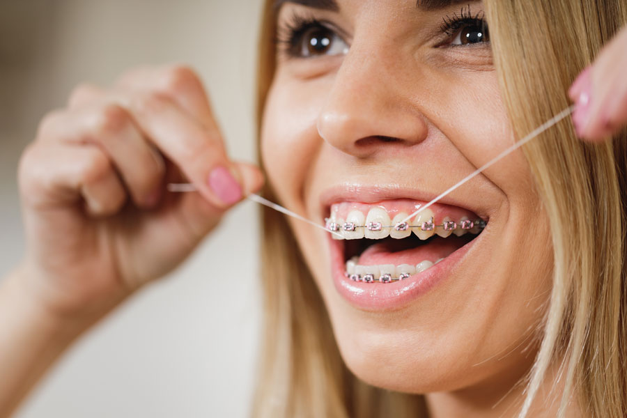 Chica limpiándose los dientes con ortodoncia con hilo dental