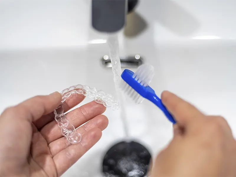 Persona limpia su ortodoncia invisible con agua y un cepillo de cerdas blandas